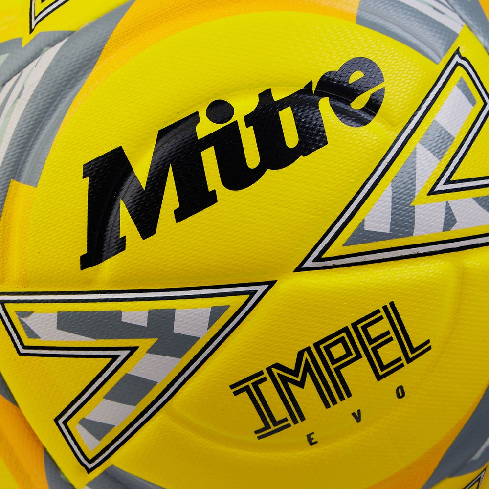 Mitre Impel Evo football resting on a turf field, showing vibrant orange and white panel design for soccer training and matches.