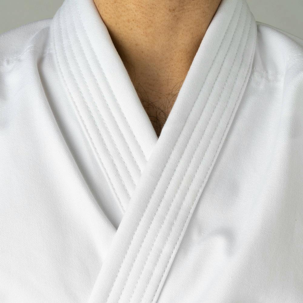 White Blitz Adult Zanshin Karate Gi made of 12oz woven cotton, shown laid flat with jacket, pants, and belt for training.