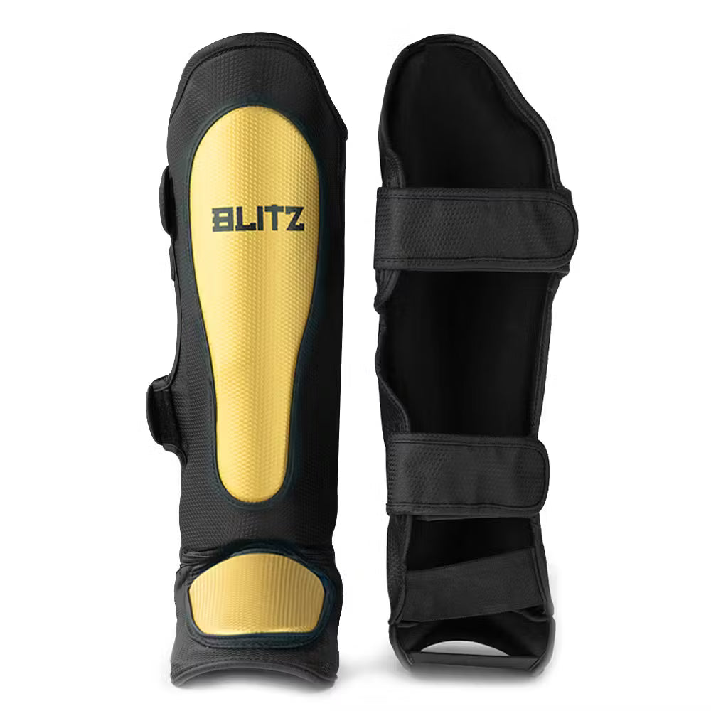 Black and gold Blitz Centurion shin guards for Muay Thai, kickboxing, and MMA, featuring padded protection and adjustable straps.