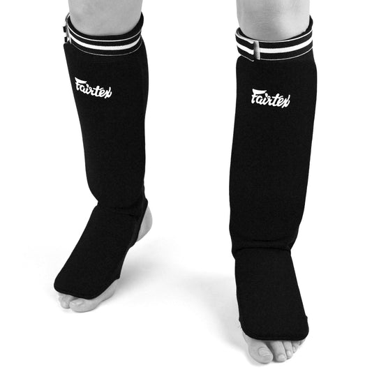 Fairtex black elastic competition shin pads for martial arts, featuring padded protection and adjustable straps.